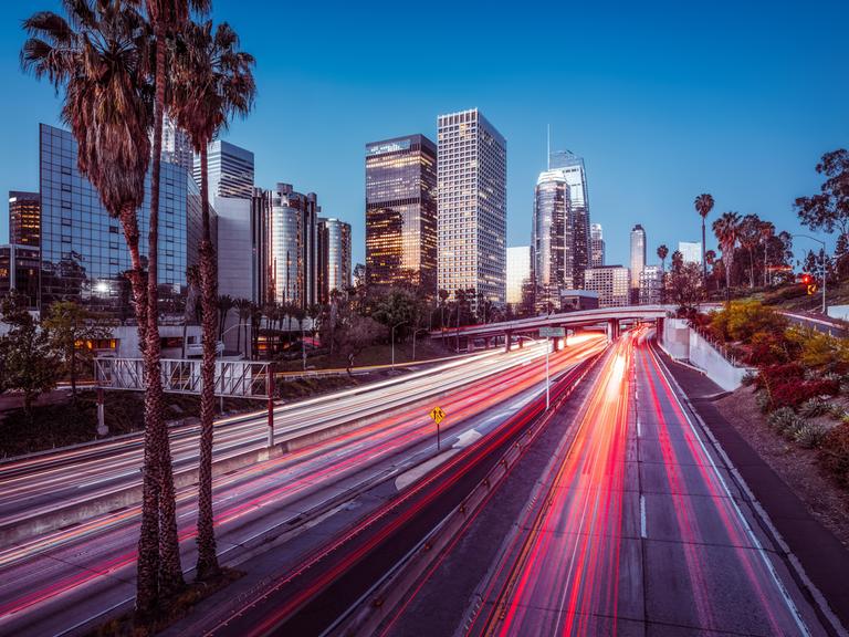 Die Skyline von Los Angeles bei Nacht mit bunt leuchtendem Highway und Wolkenkratzern.