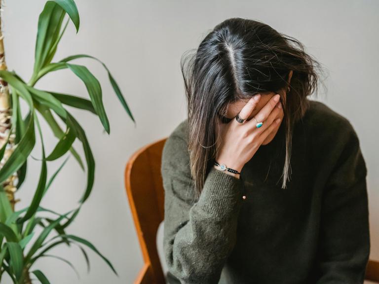 Eine Frau halt sich eine Hand vor ihr Gesicht, als ob sie resignieren würde oder ihr etwas unangehm wäre.