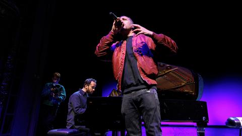 Danger Dan singt stehend in ein Mikrofon. Im Hintergrund sitzt Igor Levit am Flügel und begleitet ihn. 