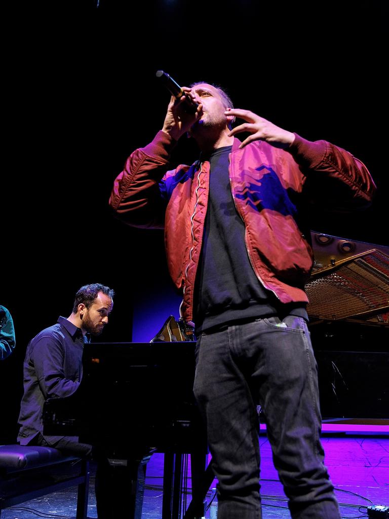 Danger Dan singt stehend in ein Mikrofon. Im Hintergrund sitzt Igor Levit am Flügel und begleitet ihn. 