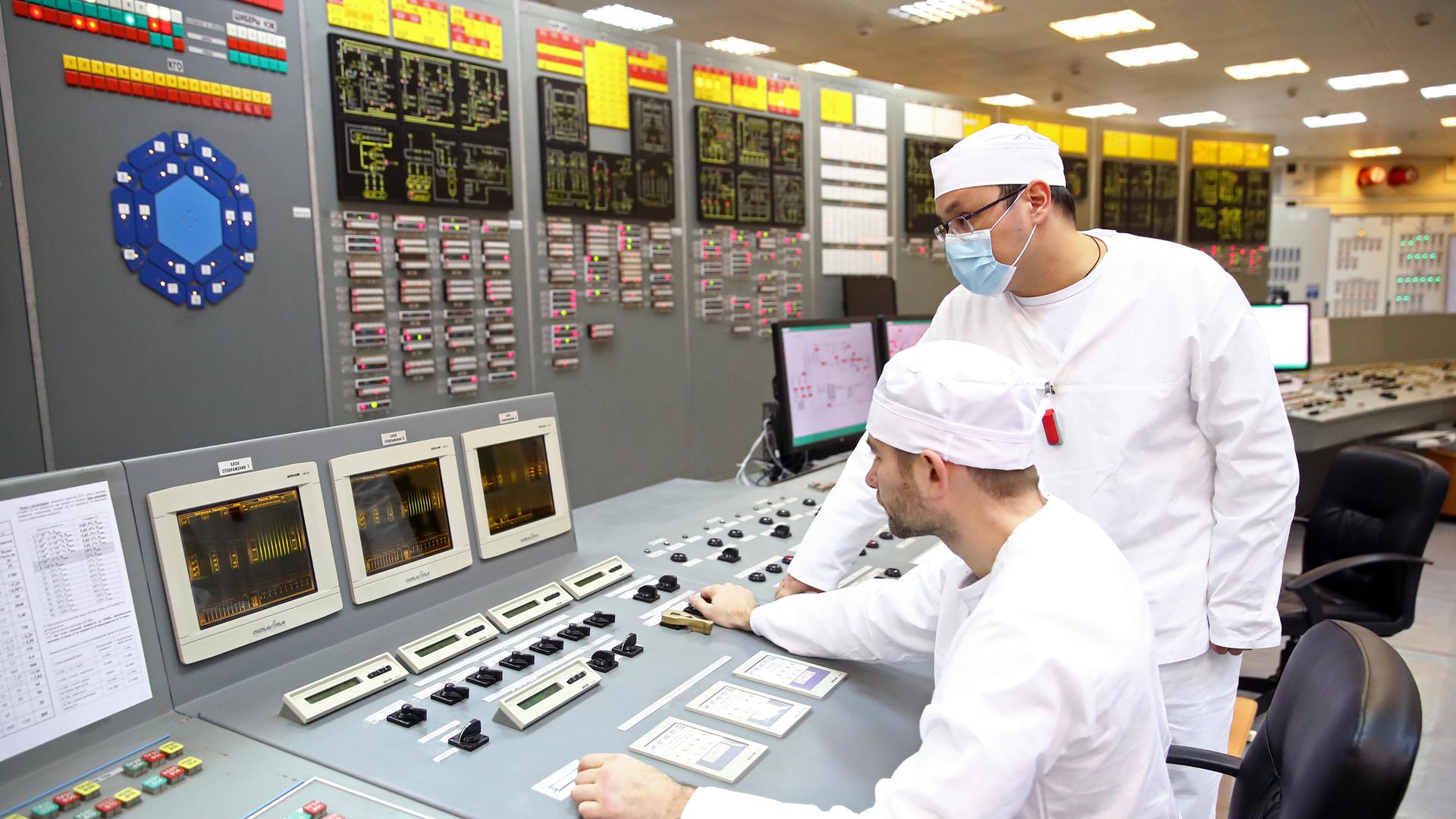 Zwei Wissenschaftler in weißen Kitteln stehen an einem Schaltpult des Forschungsreaktors PIK 