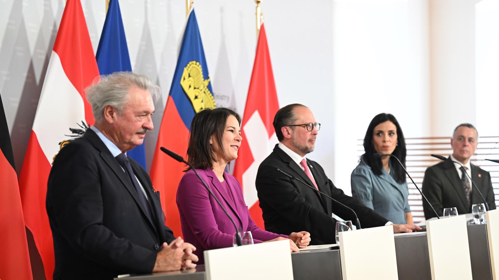 drei Männer und zwei Frauen stehen an Rednerpulten vor den Flaggern ihrer jeweiligen Länder: Luxemburg, Deutschland, Österreich, Liechtenstein und Schweiz.