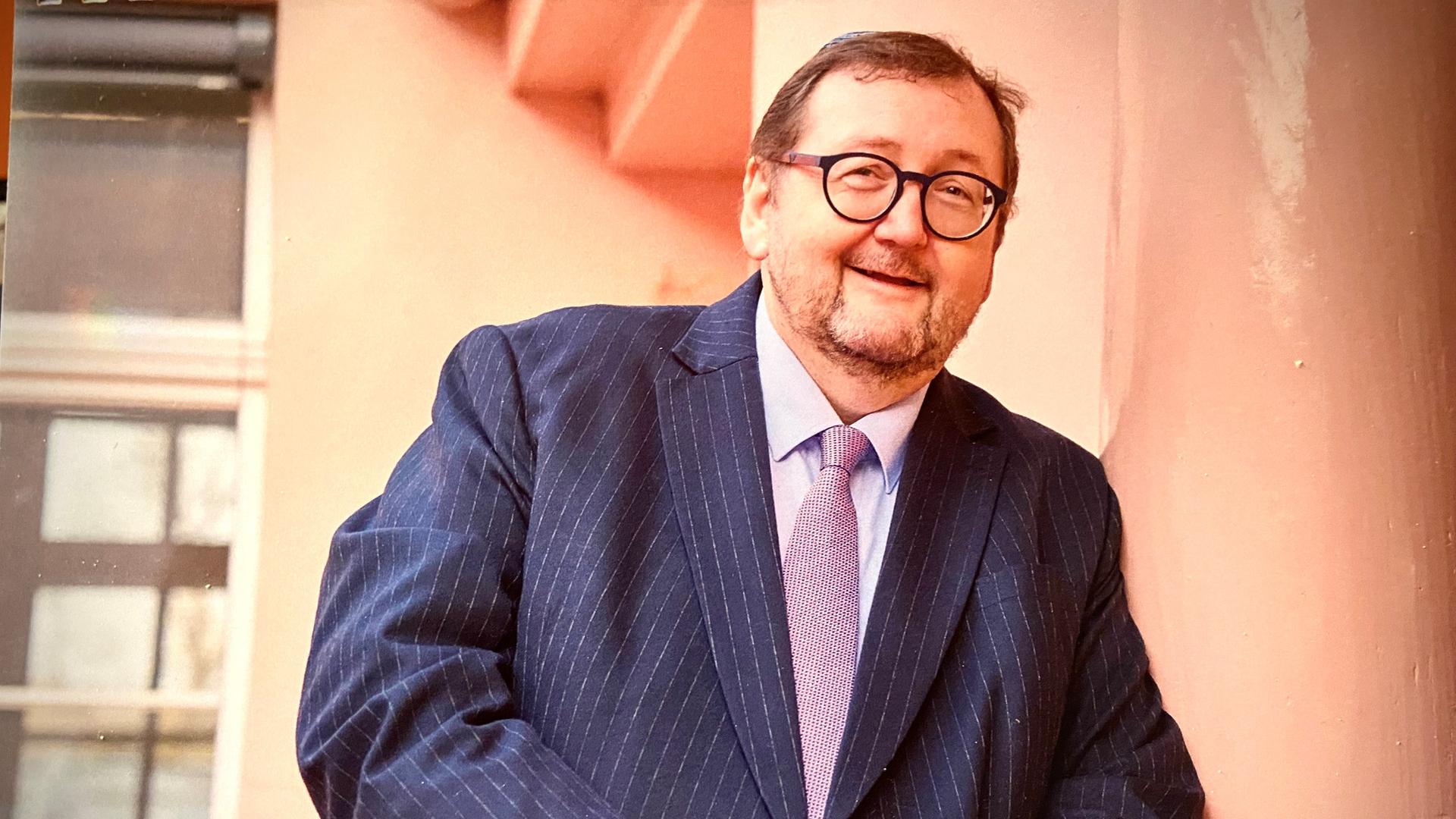 Der Rabbiner Walter Homolka, im Sakko und mit runder Brille, lehnt lächelnd an einer Wand. Der Rabbiner Walter Homolka, im Sakko und mit runder Brille, lehnt lächelnd an einer Wand.