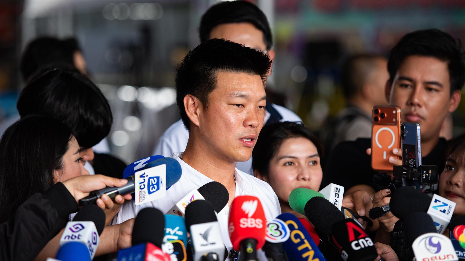 Natthaphong Ruengpanyawut steht vor vielen verschiedenen Mikrofonen, er ist umringt von Menschen.