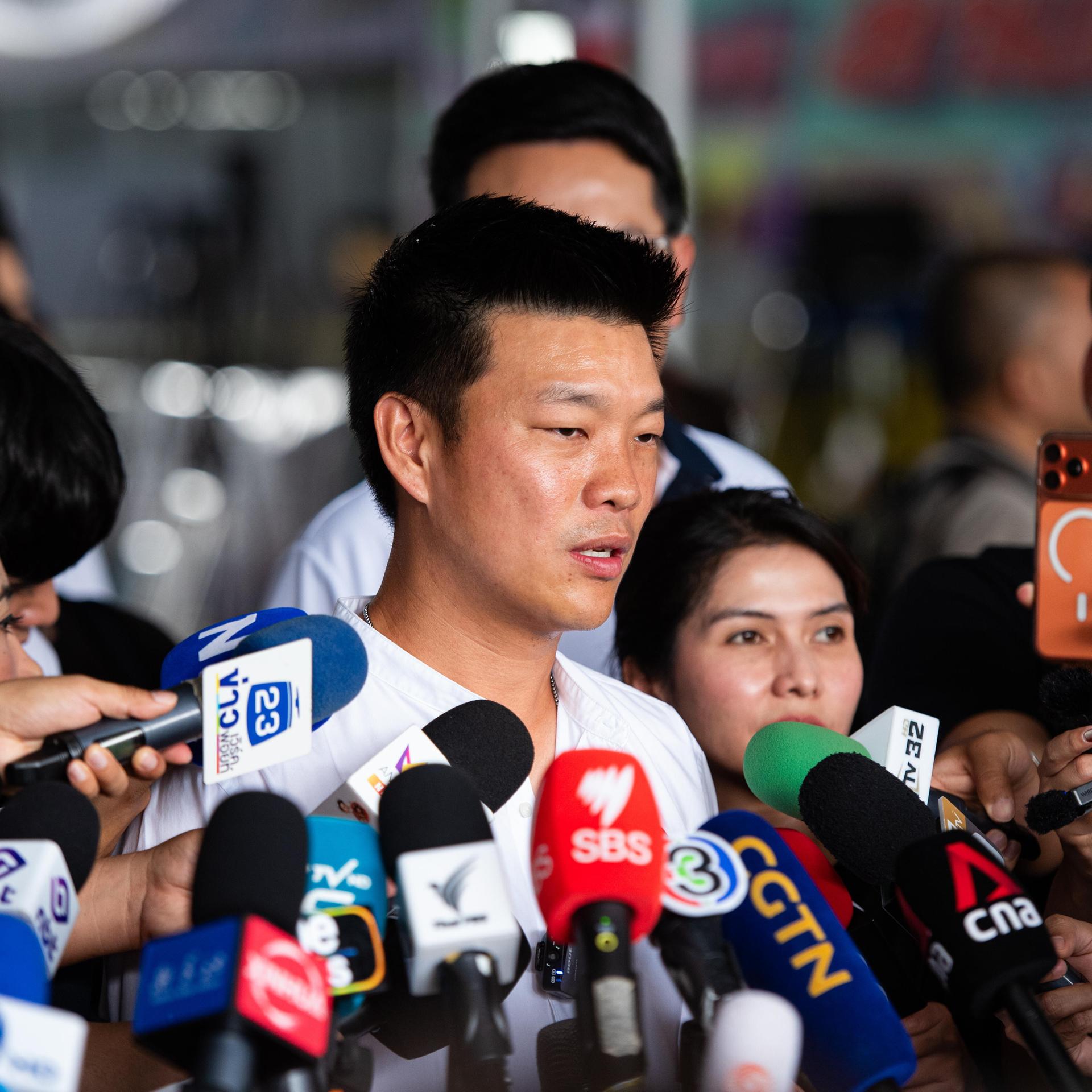 Natthaphong Ruengpanyawut steht vor vielen verschiedenen Mikrofonen, er ist umringt von Menschen.