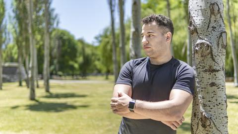 Ein junger Mann lehnt sich an einen Baum. Er blickt nachdenklich zur Seite.