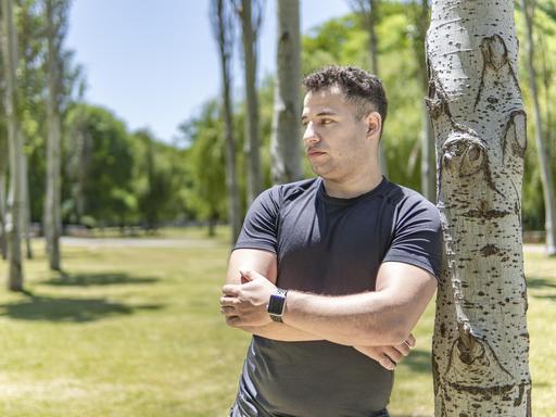Ein junger Mann lehnt sich an einen Baum. Er blickt nachdenklich zur Seite.