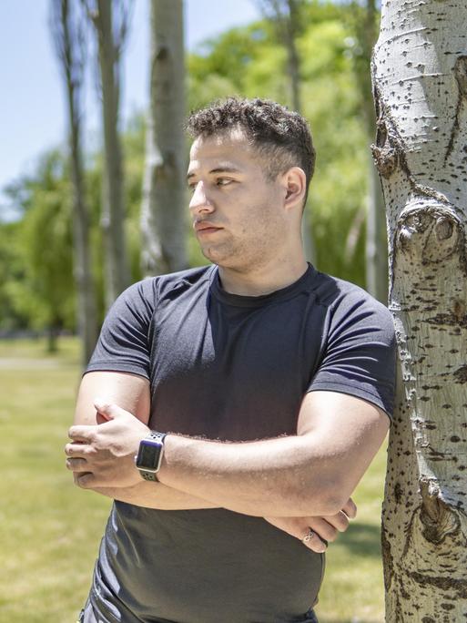 Ein junger Mann lehnt sich an einen Baum. Er blickt nachdenklich zur Seite.