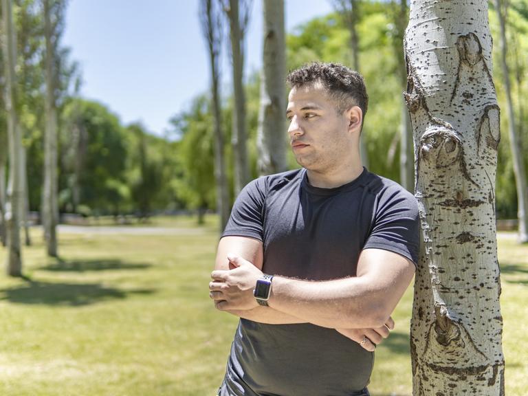 Ein junger Mann lehnt sich an einen Baum. Er blickt nachdenklich zur Seite.