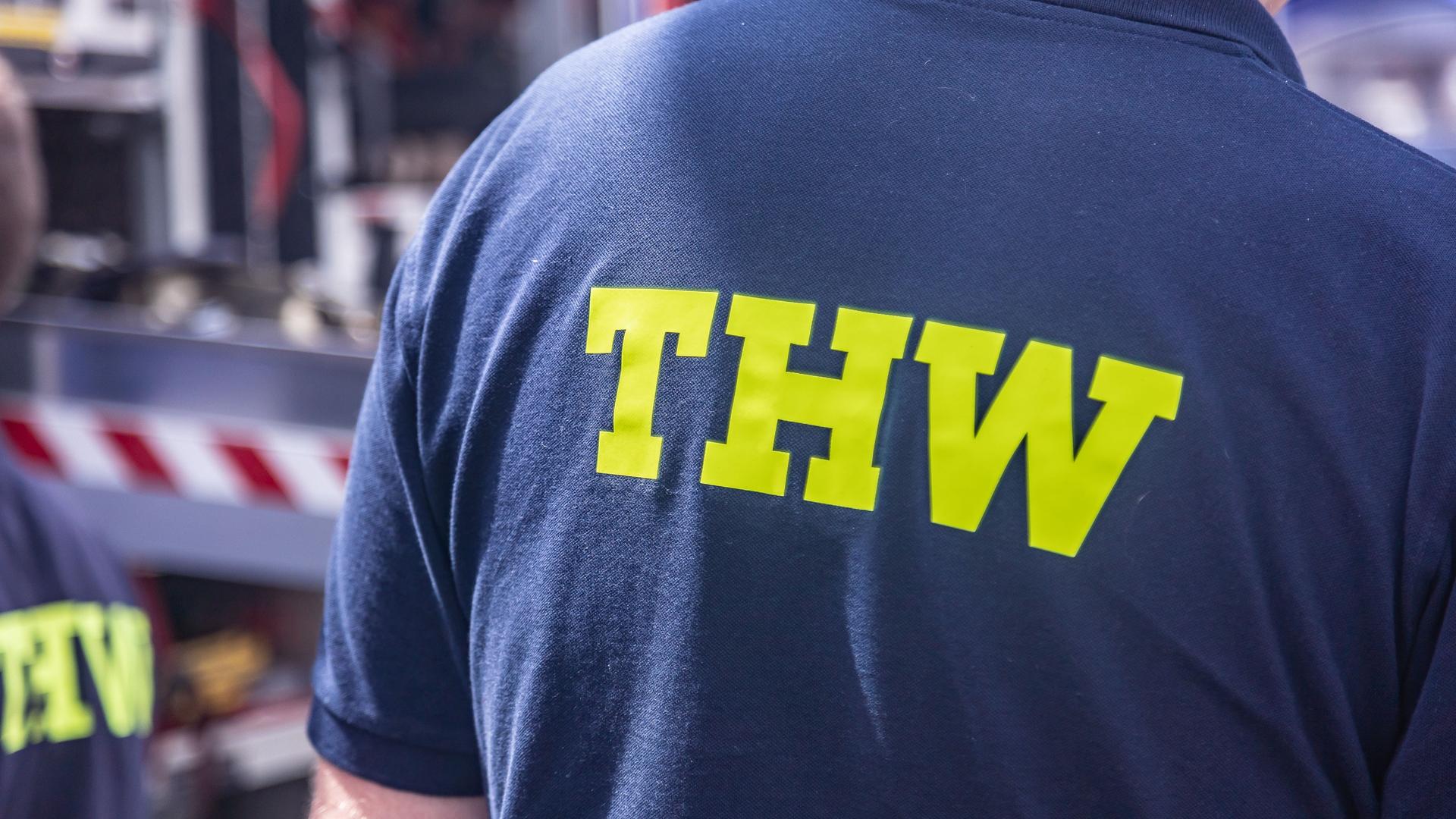 Blick auf den Rücken eines Freiwilligen beim Technischen Hilfswerk. Auf dem blauen Pullover steht in gelber Schrift "THW".