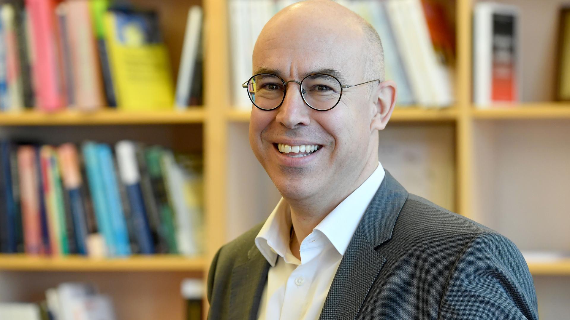 Gabriel Felbermayr, lächelt in die Kamera. Hinter ihm steht ein Bücherregal. Gabriel Felbermayr, lächelt in die Kamera. Hinter ihm steht ein Bücherregal.