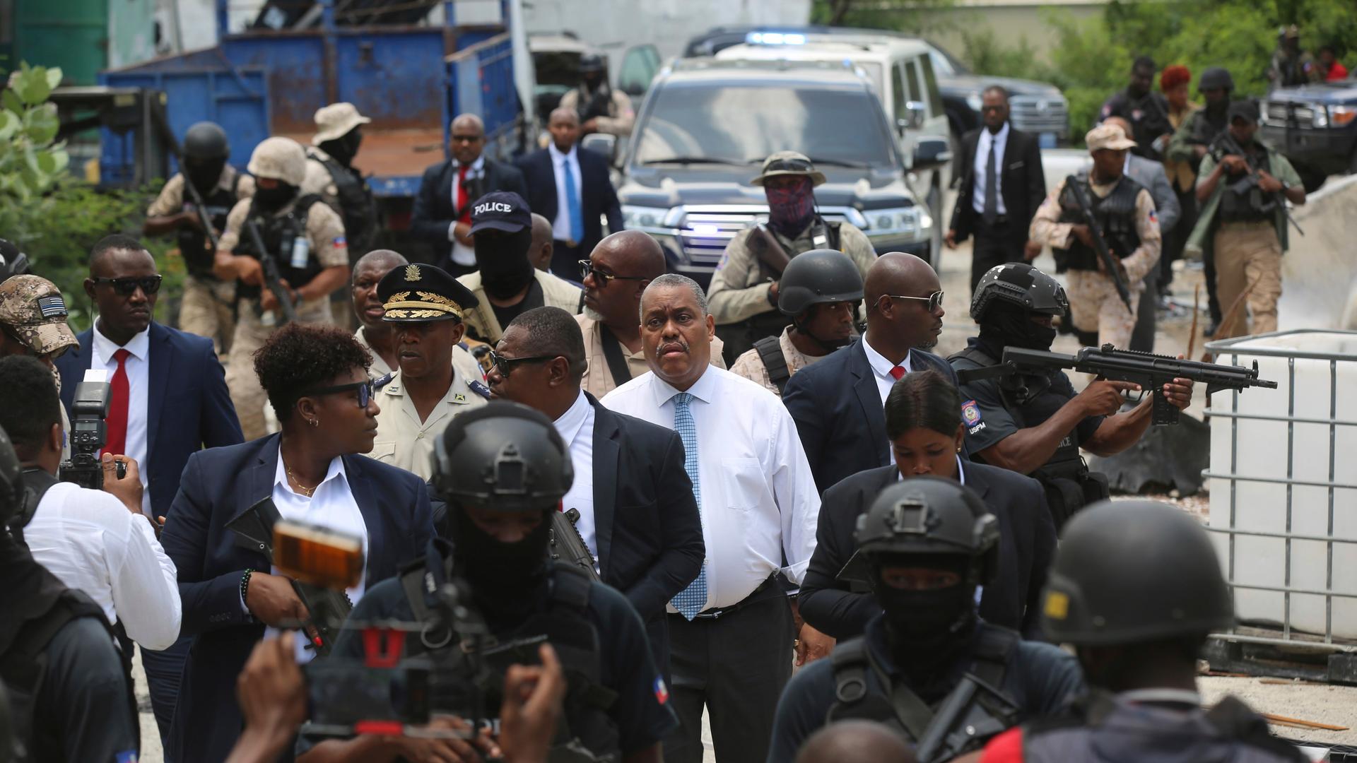 Haitis Premierminister Garry Conille, Mitte, und Polizeichef Normil Rameau, Mitte links, sind von vielen Menschen umgeben, als sie vor dem zurückeroberten Krankenhaus in Port-au-Prince stehen.