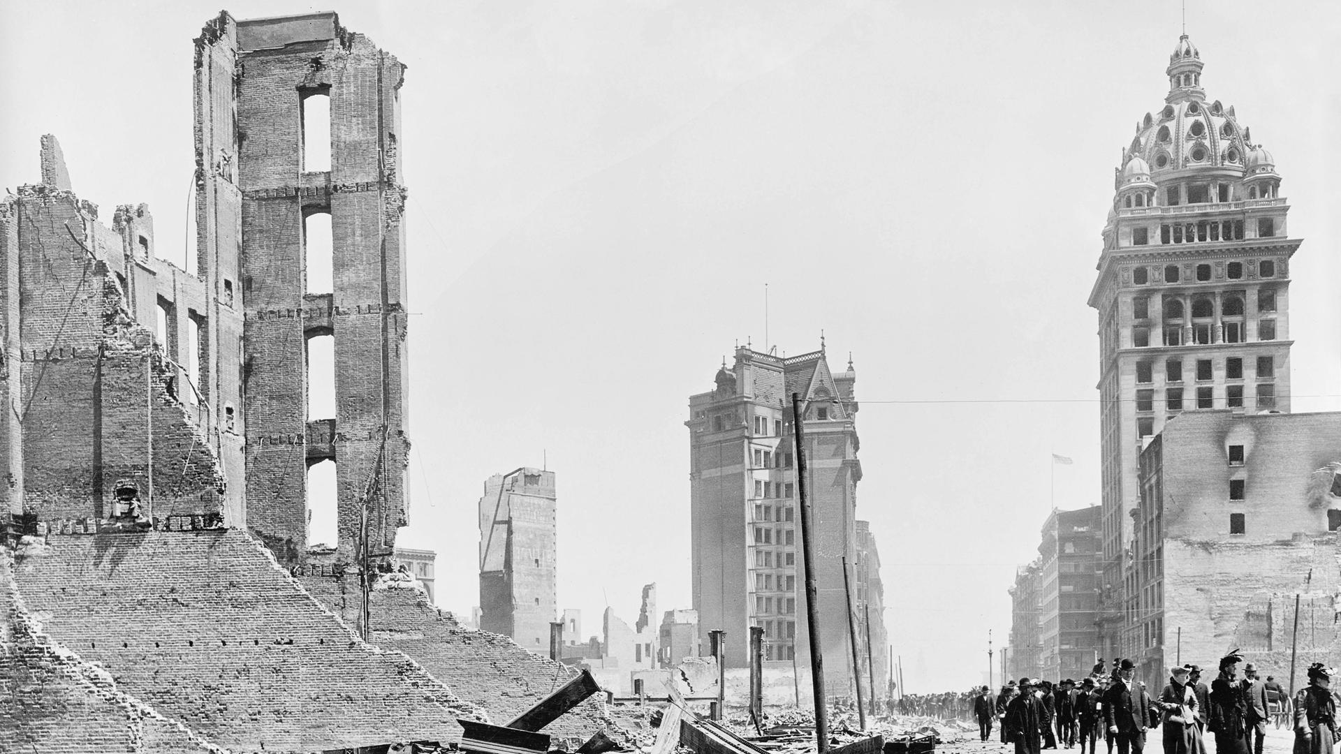 Eine Gruppe von Menschen geht eine von Trümmern gesäumte Straße entlang. (Schwarz-weiß-Fotografie)