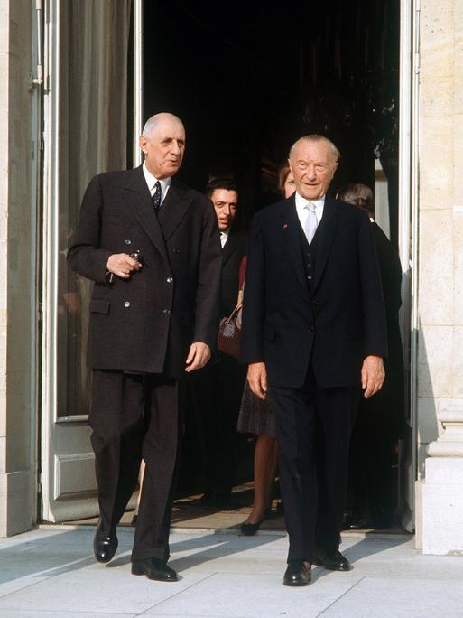Der französische Staatspräsident Charles de Gaulle und der deutsche Bundeskanzler Konrad Adenauer am 9. Februar 1961, beide in schwarzen Anzügen, vor der offenen Tür des Pariser Elysee Palastes. 