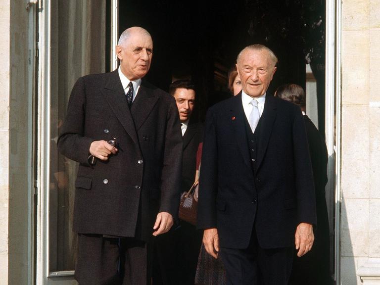 Der französische Staatspräsident Charles de Gaulle und der deutsche Bundeskanzler Konrad Adenauer am 9. Februar 1961, beide in schwarzen Anzügen, vor der offenen Tür des Pariser Elysee Palastes. 