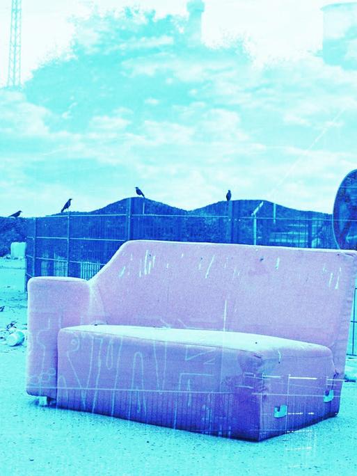 Ein rosa Sofa auf einer Art Müllkippe, im Hintergrund Berge, blau eingefärbt