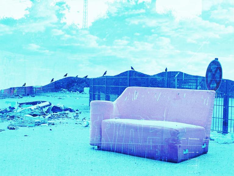 Ein rosa Sofa auf einer Art Müllkippe, im Hintergrund Berge, blau eingefärbt