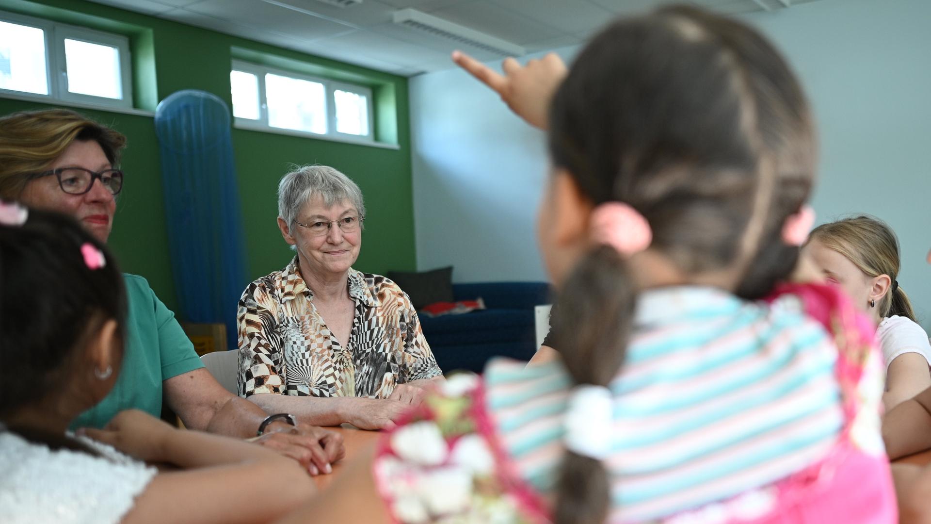 Zwei Seniorinnen sitzen mit Kindern an einem Tisch in einer Grundschule.