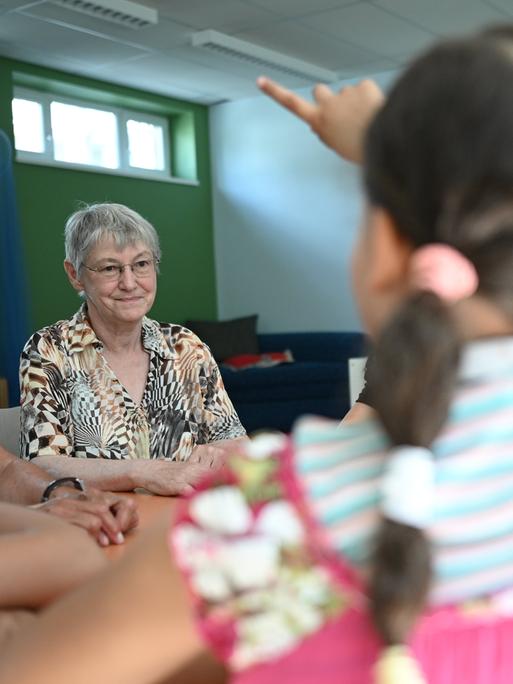 Zwei Seniorinnen sitzen mit Kindern an einem Tisch in einer Grundschule.