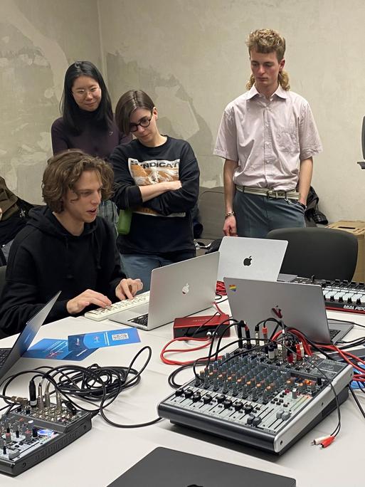 Studierende der Stuttgarter Kompositionsklasse sitzen zusammen um einen Tisch mit elektronischen Gerätschaften