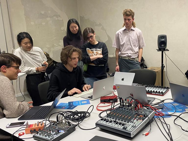 Studierende der Stuttgarter Kompositionsklasse sitzen zusammen um einen Tisch mit elektronischen Gerätschaften