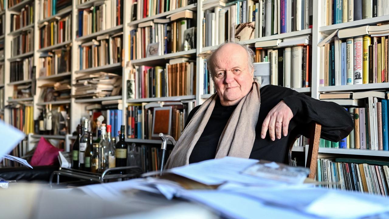 Der Komponist Wolfgang Rihm sitzt in einem Zimmer voller Bücher. Er sitzt auf einem Stuhl, den linken Arm auf dessen Lehne abgelegt, und schaut in die Kamera. Er hat eine Halbglatze und etwas längeres Haar. Er trägt ein schwarzes Hemd und hat einen hellbraunen Schal umgelegt. Vor ihn liegen auf dem Flügel zahlreiche Hefte und Papiere. 