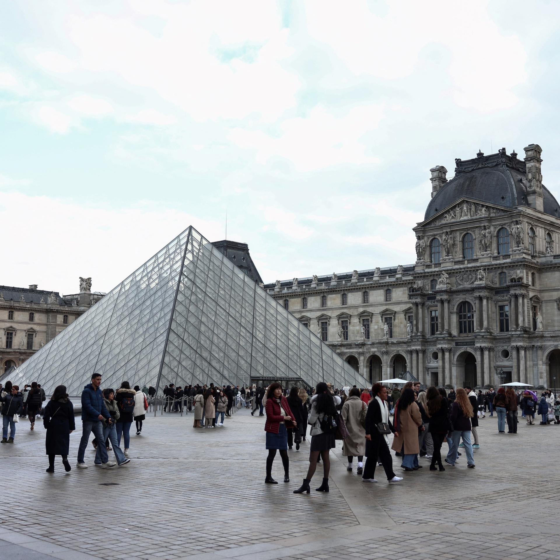 In der Nähe der Louvre-Pyramide, die vom chinesisch-amerikanischen Architekten Ieoh Ming Pei entworfen wurde, flanieren Touristen am 28. Februar 2025 in Paris.