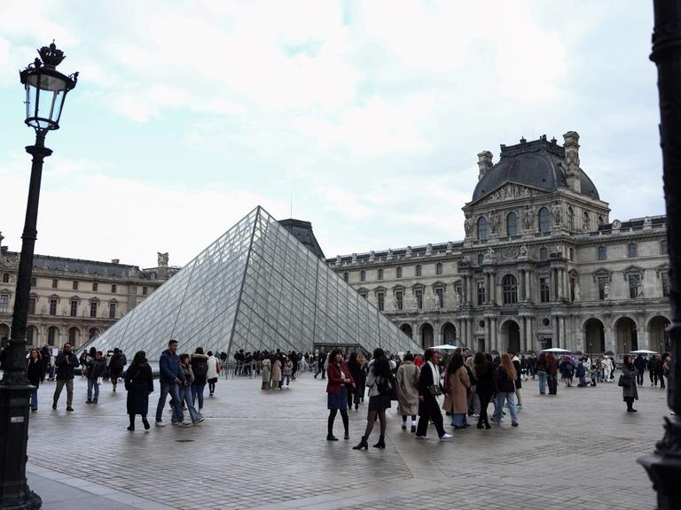 In der Nähe der Louvre-Pyramide, die vom chinesisch-amerikanischen Architekten Ieoh Ming Pei entworfen wurde, flanieren Touristen am 28. Februar 2025 in Paris.