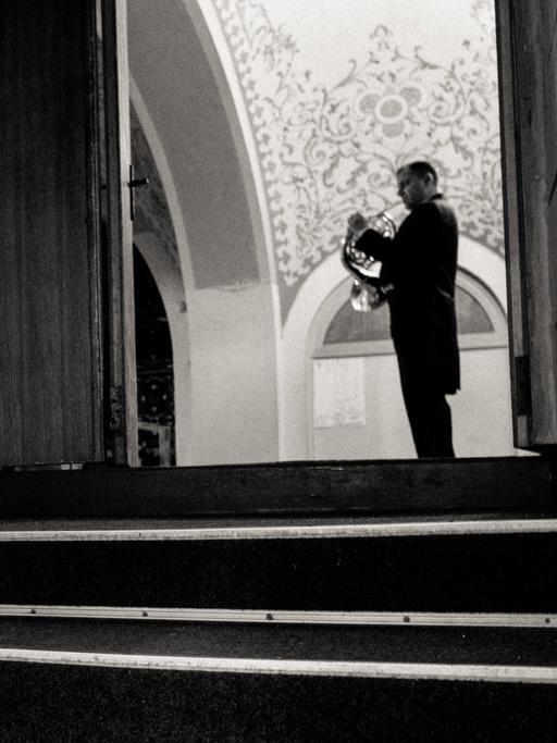 Im Erdgeschoss der Konzerthalle Odessa hat ein Hornist sein Instrument auf einer Treppe abgelegt. Ein weiterer spielt in der großen Halle, die sich am Ende der Treppe eröffnet.