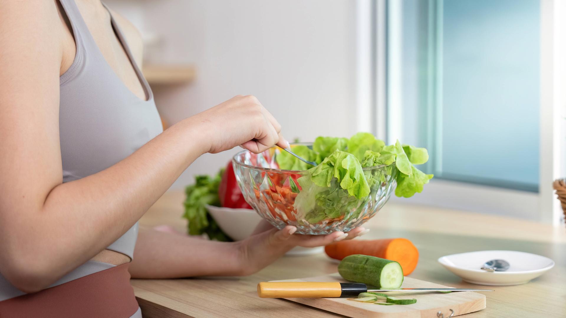 Eine Frau trägt ein Trainingsoutfit und bereitet einen Salat vor.