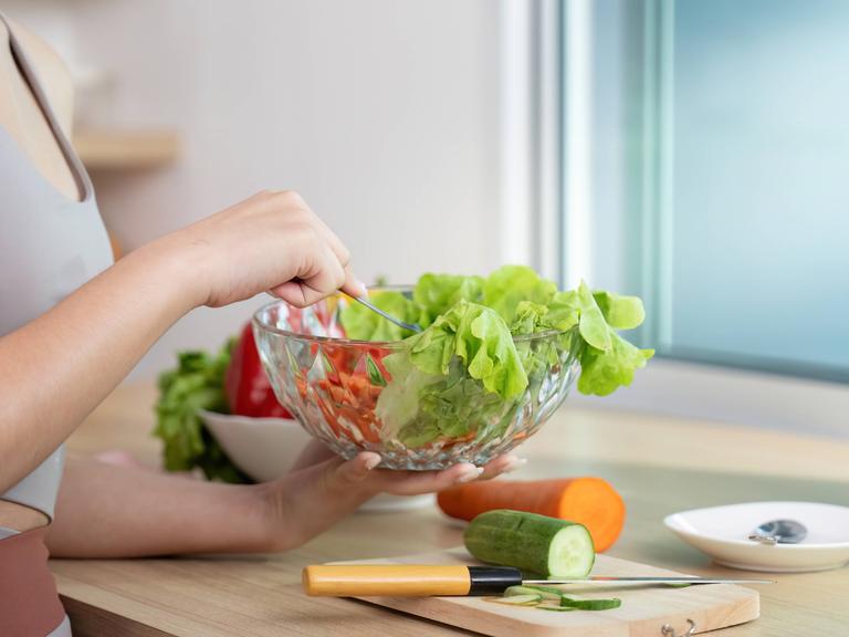 Eine Frau trägt ein Trainingsoutfit und bereitet einen Salat vor.
