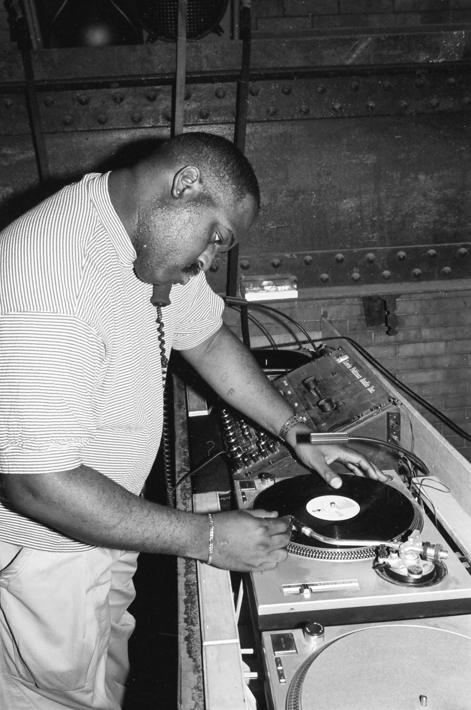 Ein Mann steht an einem DJ-Pult und legt den Arm mit der Nadel auf eine Platte.
