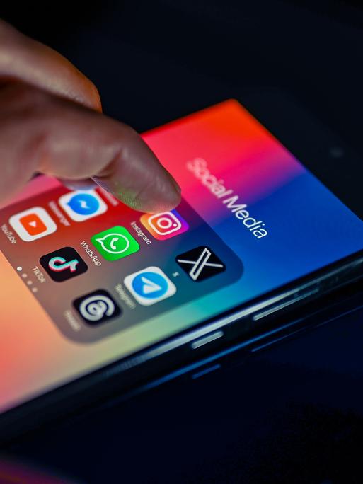 Eine Hand wischt über Social-Media-Icons auf einem Smartphone.