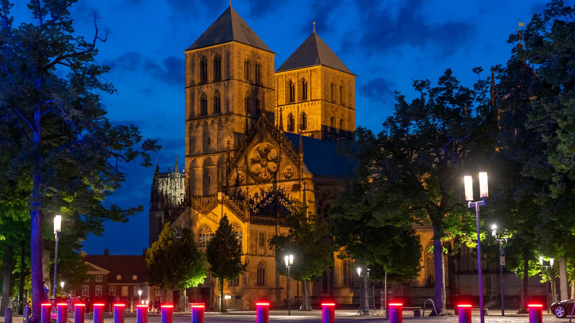 Sankt-Paulus-Dom in der Altstadt Münster in der Dämmerung mit roten Warnlichtern an Pollern davor.