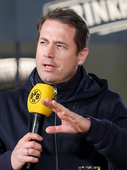Lars Ricken spricht in ein gelbes Mikrofon mit BVB-Logo.