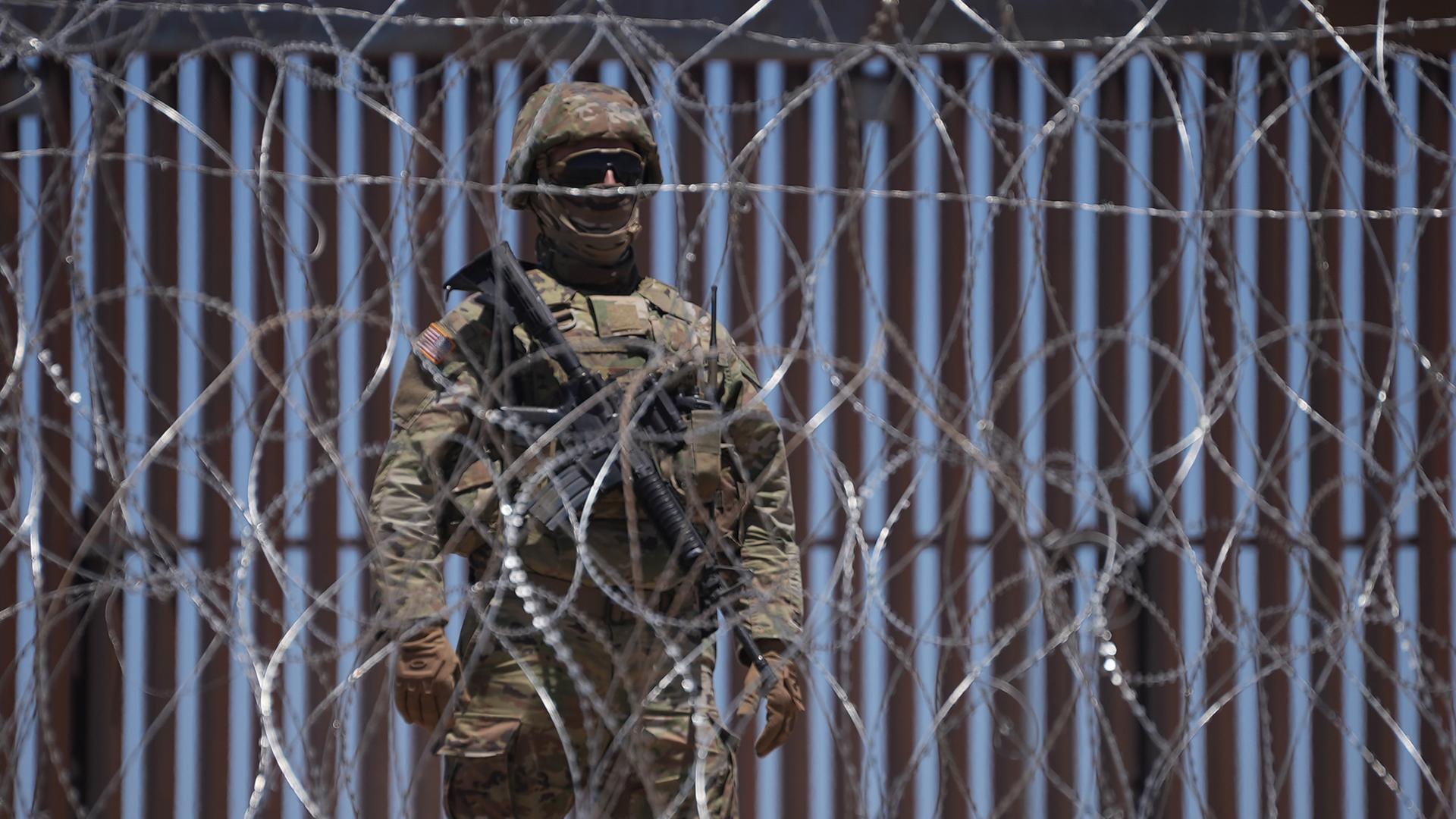 Schwerbewaffnete Sicherheitskräfte stehen hinter einem Stacheldrahtzaun an der Grenze zwischen Mexiko und USA. 