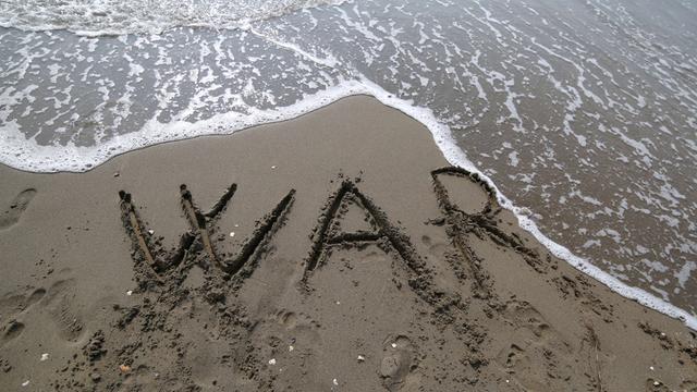 Die Buchstaben "W A R" sind in den Sand an einem Strand geschrieben.