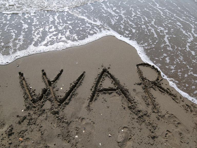 Die Buchstaben "W A R" sind in den Sand an einem Strand geschrieben.