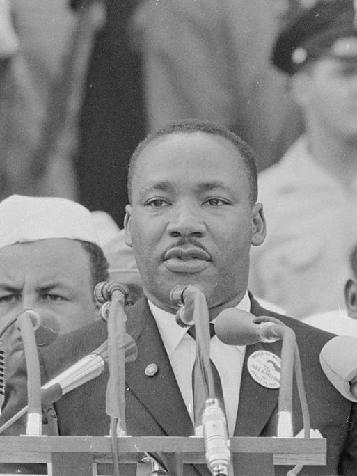 Martin Luther King steht auf einer öffentlichen Bühne und hält eine Rede