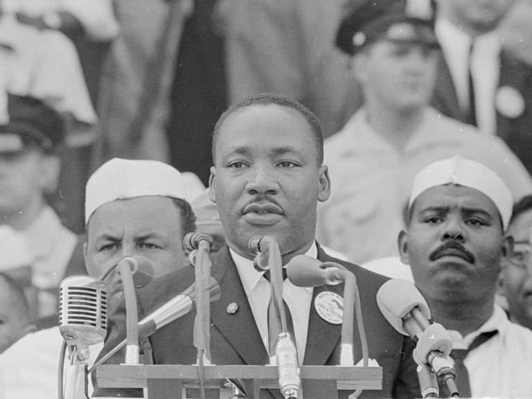 Martin Luther King steht auf einer öffentlichen Bühne und hält eine Rede