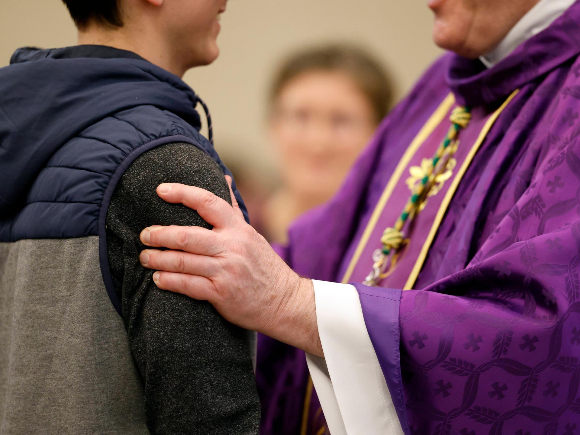 Ein katholischer Priester spricht mit einem jungen Taufbewerber in Frankreich. Zu sehen ist die Hand des Priesters auf dem Arm des jungen Mannes.