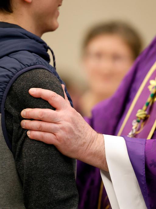 Ein katholischer Priester spricht mit einem jungen Taufbewerber in Frankreich. Zu sehen ist die Hand des Priesters auf dem Arm des jungen Mannes.