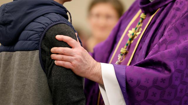 Ein katholischer Priester spricht mit einem jungen Taufbewerber in Frankreich. Zu sehen ist die Hand des Priesters auf dem Arm des jungen Mannes.