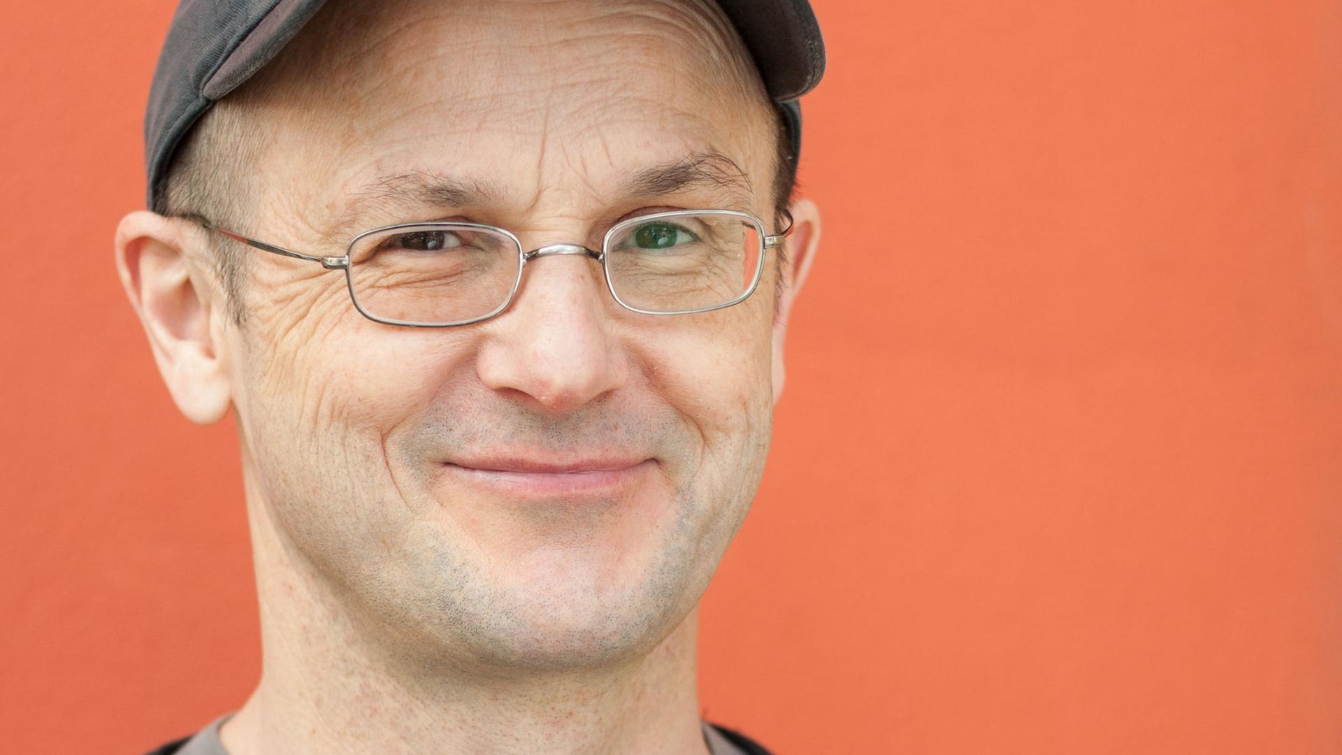 Autor Steffen Mensching lächelnd und mit Baskenmütze vor einer orangenen Wand