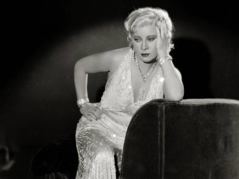 Eine historische schwarzweiss Aufnahme der Hollywood-Schauspielerin Mae West in einem glitzernden Abendkleid.