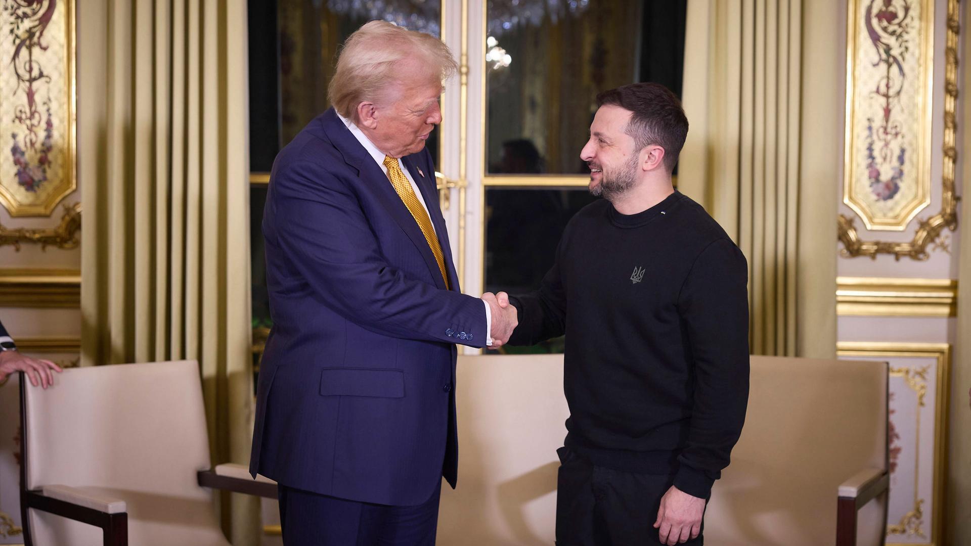 US-Präsident Trump und Ukraines Präsident Selenskyj geben sich die Hand. Sie stehen in einem Raum im Élysée-Palast in Frankreich.