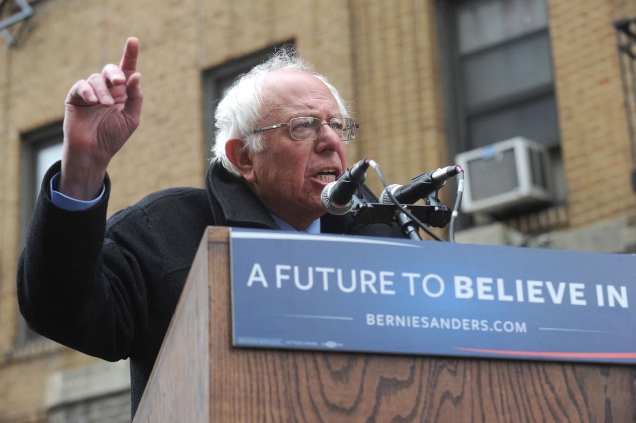 Bernie Sanders am Rednerpult, daran ist ein Schild mit der Aufschrift "A future to believe in - berniesanders.com" befestigt.