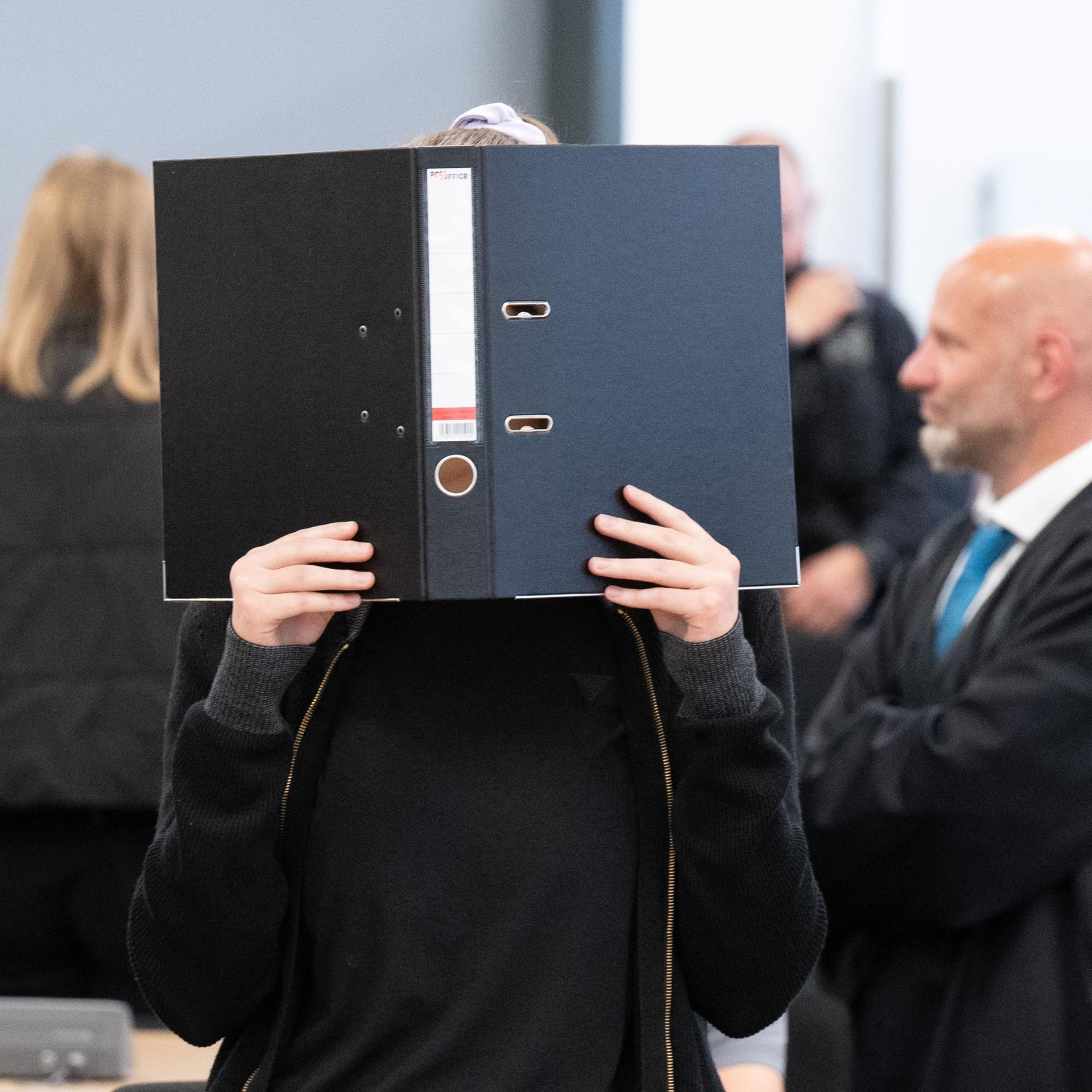 Die Angeklagte Lina E. steht bei der Fortsetzung des Prozesses im Oberlandesgericht (OLG) Dresden im Verhandlungssaal und hält einen Aktenordner vor ihr Gesicht. Das Oberlandesgericht hat die mutmaßliche Linksextremistin Lina E. zu fünf Jahren und drei Monaten Freiheitsstrafe verurteilt. Nach Auffassung des Gerichts gehörte sie einer Gruppe an, die Überfälle auf Mitglieder der rechten Szene begangen hat.