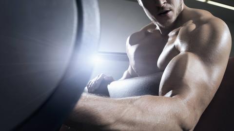 Ein Mann mit viel Muskelmasse trainiert mit Hanteln im Fitnessstudio
