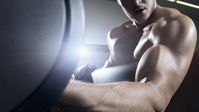 Ein Mann mit viel Muskelmasse trainiert mit Hanteln im Fitnessstudio